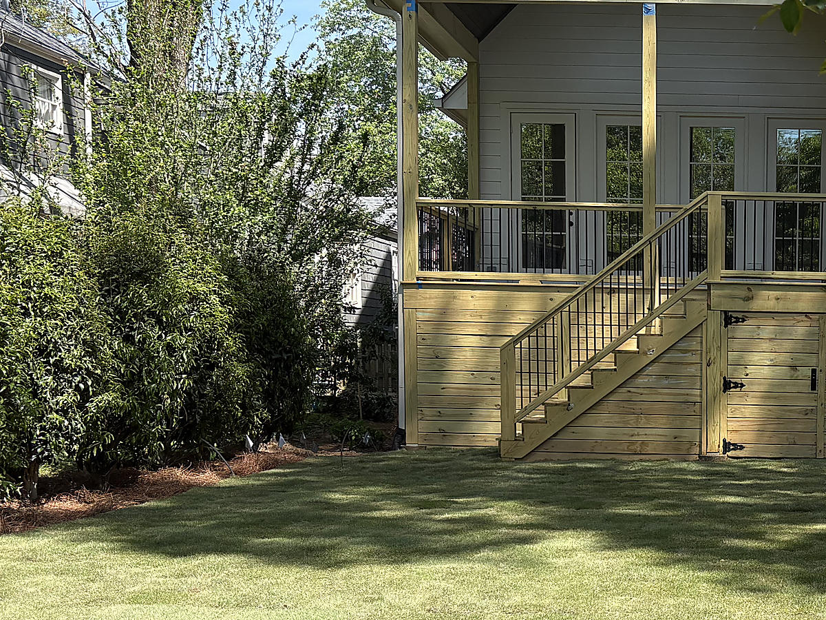 Finished lawn and mulched planting beds beside a raised porch and wooden steps