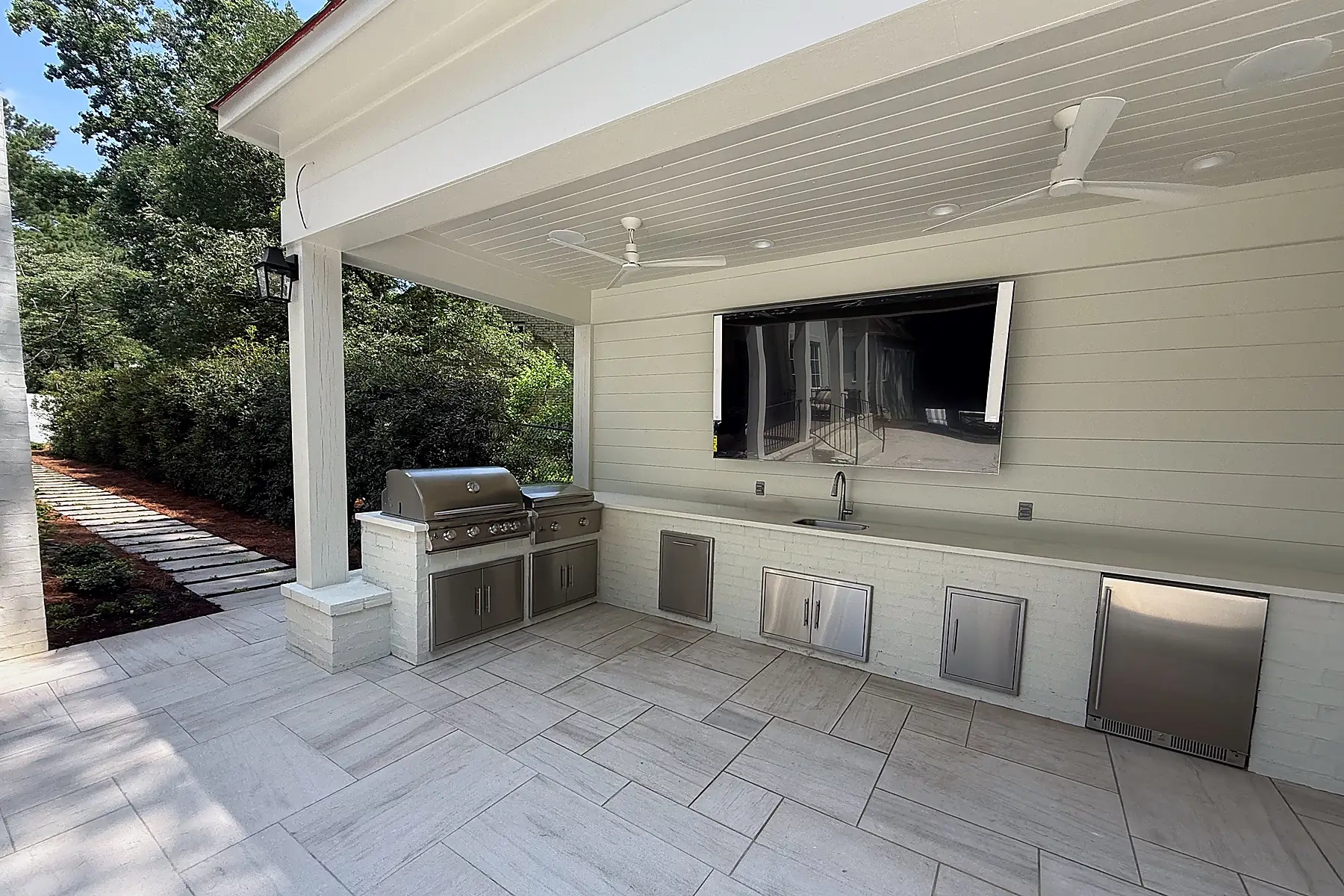 Covered outdoor kitchen with a built-in grill, sink, stainless steel storage, and stone paving