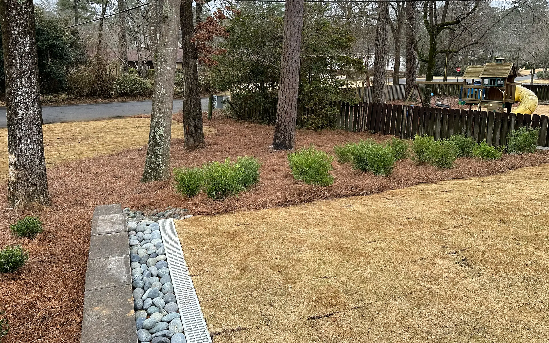 Completed drainage installation with trench drain, river rock, and finished lawn edge